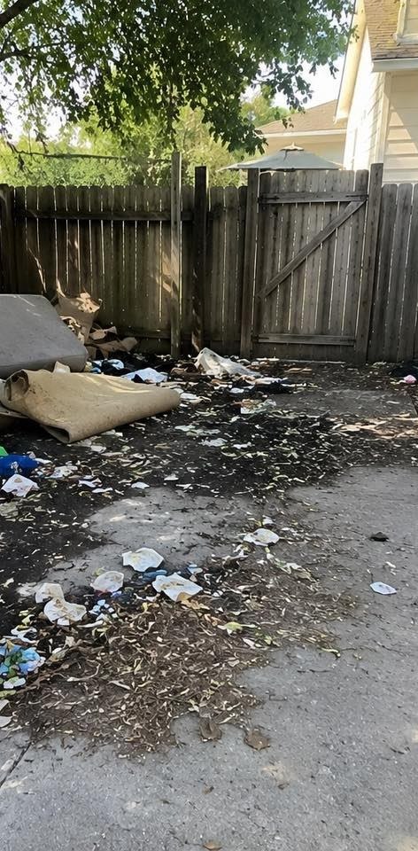 A back patio covered in scattered trash, leaves, and an abandoned rolled carpet