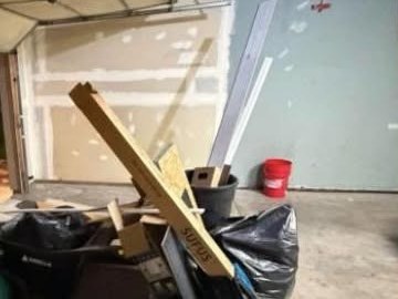 Garage bay stacked with lumber, drywall offcuts, and bagged waste