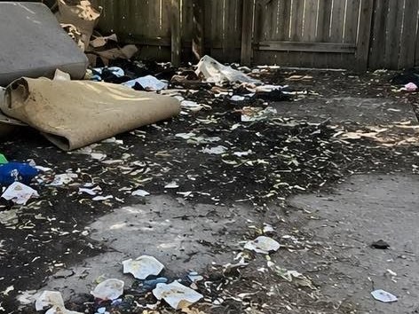 Back patio covered in scattered trash, leaf litter, and an old rolled carpet