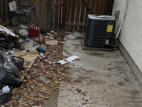 Side yard strewn with bagged waste, a broken cart, and years of litter